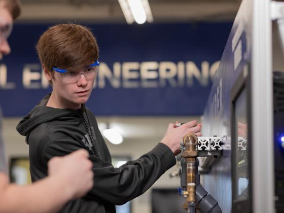 Student working on a copper pipe in with an engineering sign in the background.