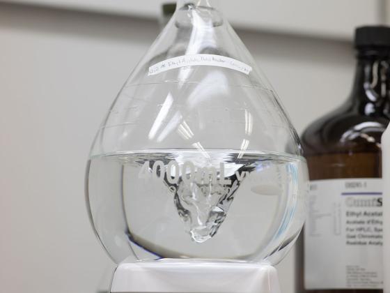 Liquid swirling in a 4000mL beaker with a brown jug of another chemical in the background.